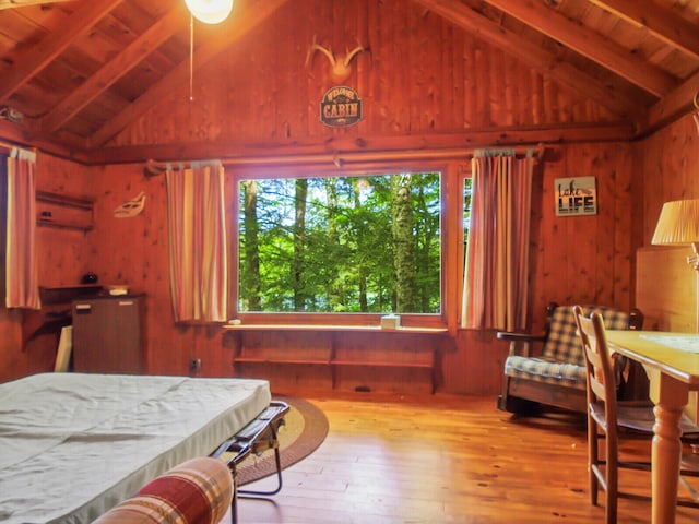 bedroom featuring wood walls, lofted ceiling with beams, hardwood / wood-style flooring, and wood ceiling