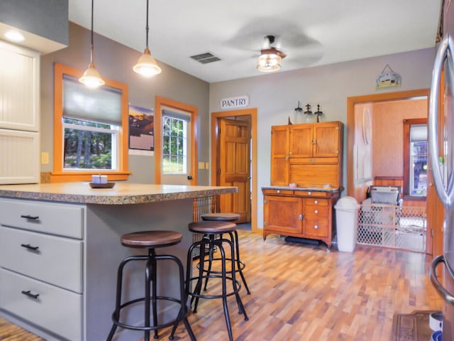 kitchen with decorative light fixtures, light hardwood / wood-style floors, gray cabinetry, ceiling fan, and a breakfast bar area