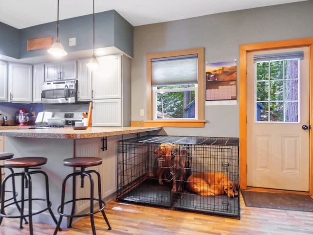 kitchen with range, a kitchen bar, hanging light fixtures, white cabinets, and hardwood / wood-style flooring