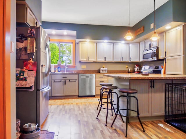 kitchen featuring stainless steel appliances, decorative light fixtures, light wood-type flooring, sink, and a kitchen bar