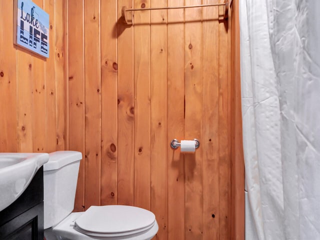 bathroom featuring wood walls, toilet, and vanity