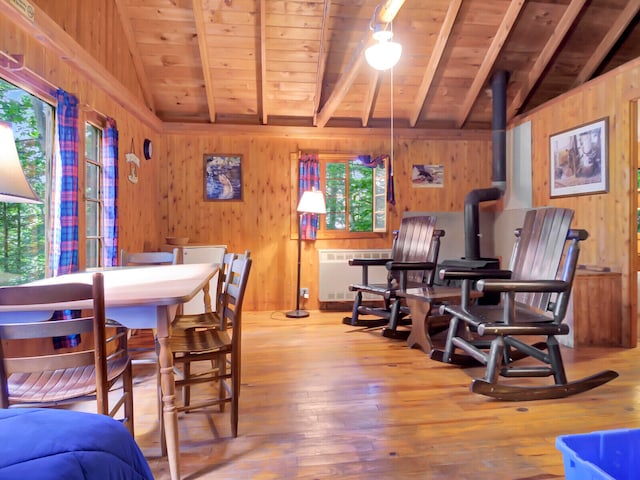 dining room with vaulted ceiling with beams, hardwood / wood-style floors, wooden walls, and radiator heating unit