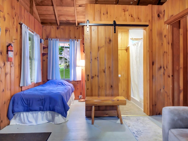 bedroom with a barn door, lofted ceiling with beams, wood walls, and wooden ceiling