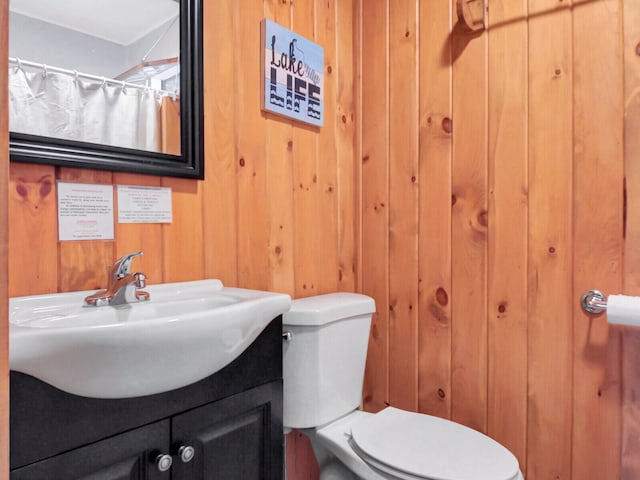 bathroom featuring wood walls, toilet, and large vanity