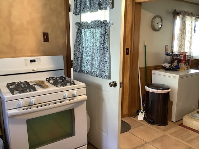 kitchen with light tile patterned floors, white gas range oven, and washer / clothes dryer