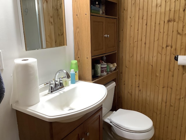 bathroom featuring vanity, wood walls, and toilet