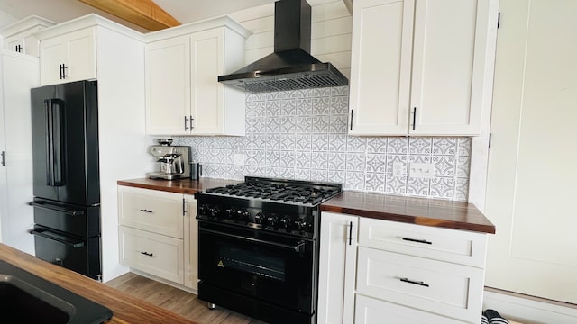 kitchen featuring wall chimney range hood, black appliances, wooden counters, and white cabinets