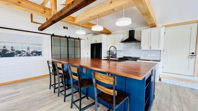 kitchen featuring sink, pendant lighting, wall chimney range hood, a barn door, and white cabinets