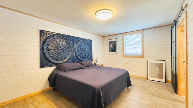 bedroom with a barn door, wooden walls, and light hardwood / wood-style flooring