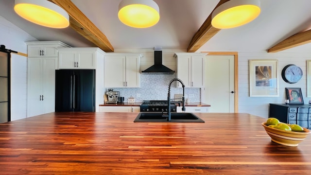 kitchen with black refrigerator, wall chimney range hood, white cabinetry, and sink