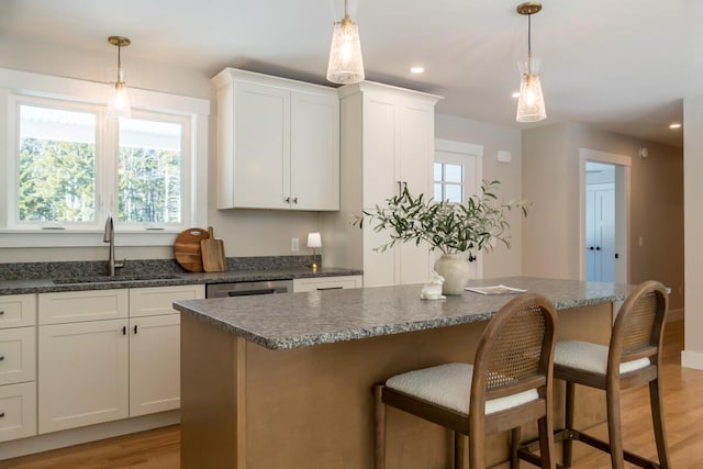 kitchen featuring light wood-style flooring, a sink, dishwasher, a kitchen breakfast bar, and a center island