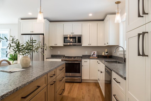 kitchen featuring a sink, dark stone countertops, stainless steel appliances, white cabinets, and light wood finished floors