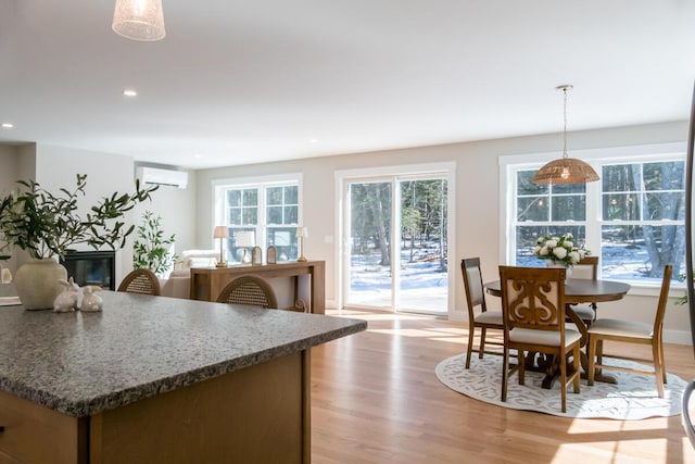 kitchen featuring decorative light fixtures, a glass covered fireplace, light wood-style floors, and a wall unit AC