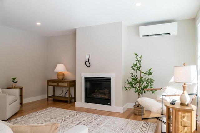 living room featuring a glass covered fireplace, a wall mounted air conditioner, baseboards, and wood finished floors