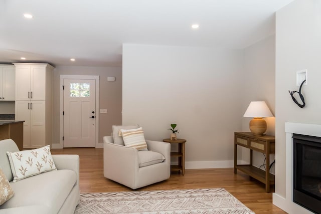 living area with a glass covered fireplace, recessed lighting, light wood-style floors, and baseboards