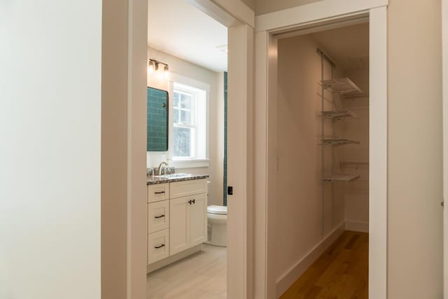 bathroom with vanity, wood finished floors, baseboards, a spacious closet, and toilet