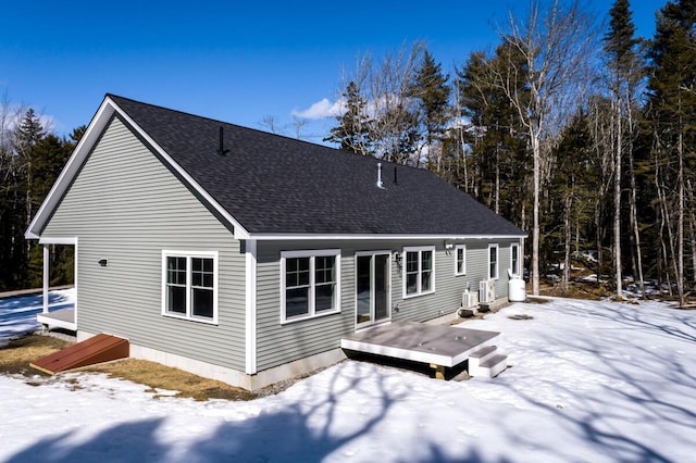 snow covered rear of property with a deck and a shingled roof