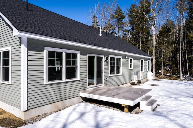 snow covered rear of property featuring a wooden deck, cooling unit, and a shingled roof