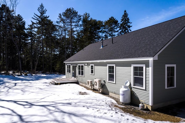 snow covered rear of property with a deck and roof with shingles