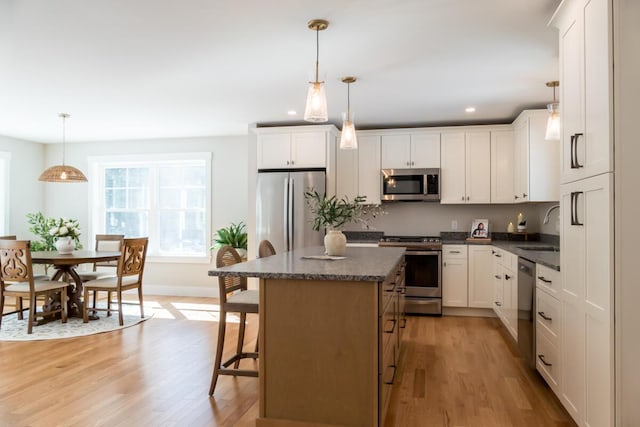 kitchen with light wood-type flooring, a sink, a kitchen breakfast bar, a kitchen island, and appliances with stainless steel finishes