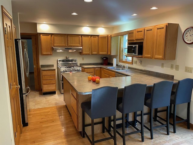 kitchen featuring a peninsula, appliances with stainless steel finishes, under cabinet range hood, and a breakfast bar