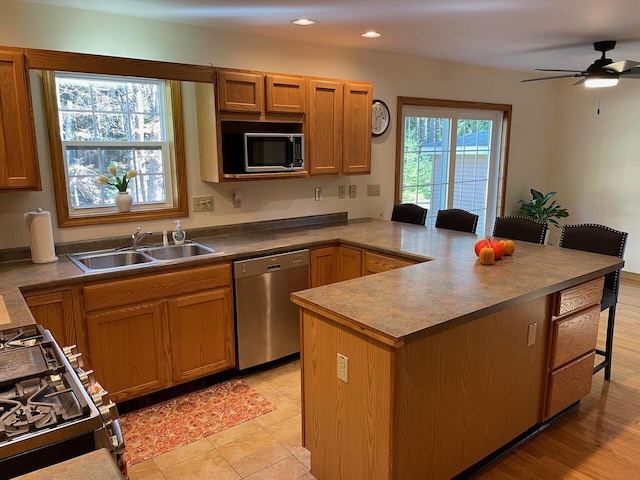 kitchen featuring a peninsula, a sink, ceiling fan, a breakfast bar, and appliances with stainless steel finishes