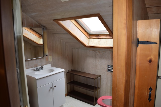 bathroom featuring vaulted ceiling with skylight, toilet, vanity, and wood walls