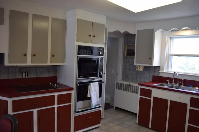 kitchen with light tile flooring, tasteful backsplash, black appliances, radiator heating unit, and sink