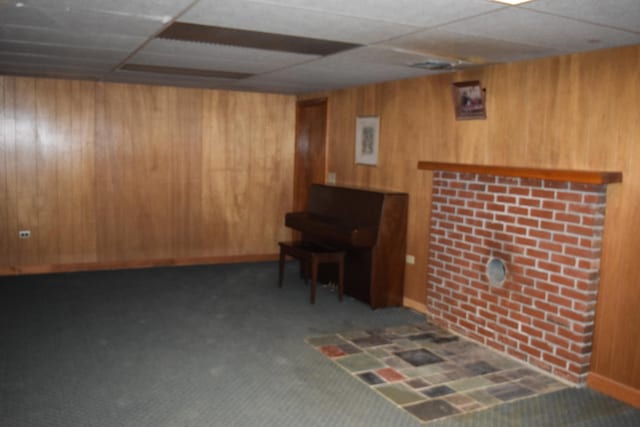 basement with wooden walls, dark colored carpet, and a paneled ceiling