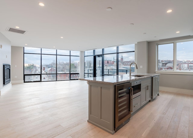 kitchen with wine cooler, a kitchen island with sink, a sink, open floor plan, and light stone countertops