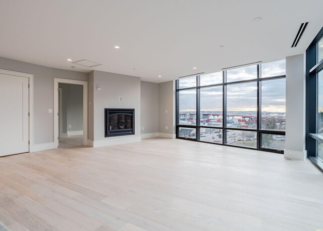 unfurnished living room featuring baseboards, visible vents, a glass covered fireplace, light wood-style floors, and floor to ceiling windows