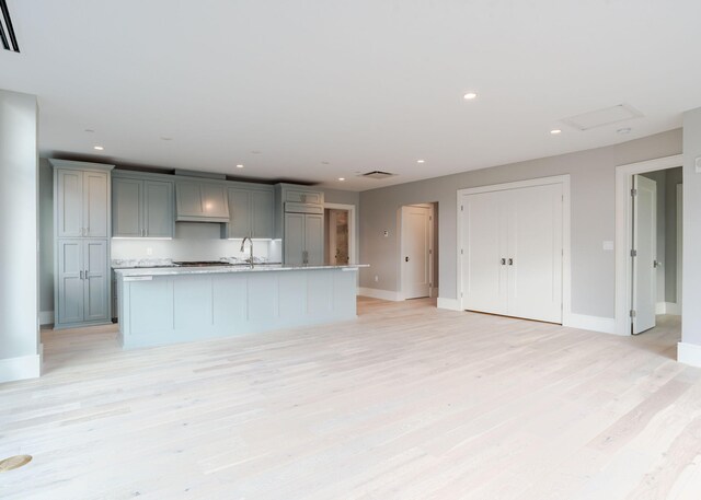 kitchen featuring recessed lighting, gray cabinets, light wood finished floors, and an island with sink