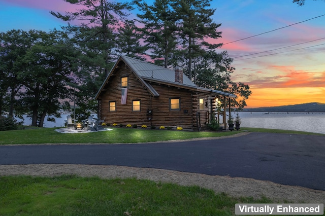 property exterior at dusk with a lawn and a water view