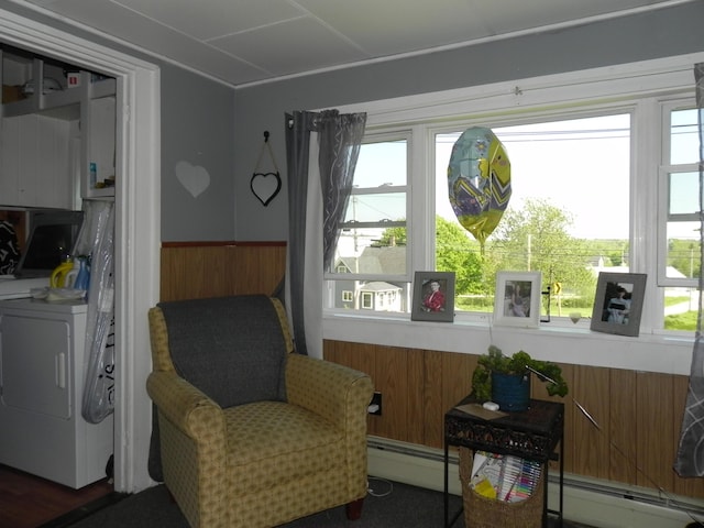 sitting room with a baseboard radiator, washer / dryer, and wood walls