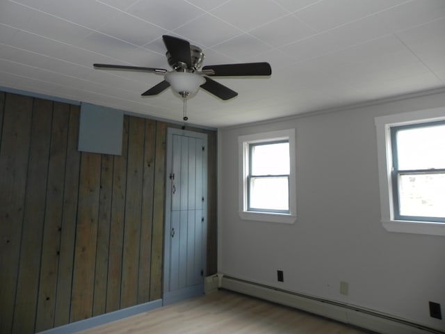 spare room with a baseboard heating unit, wooden walls, wood finished floors, and ceiling fan