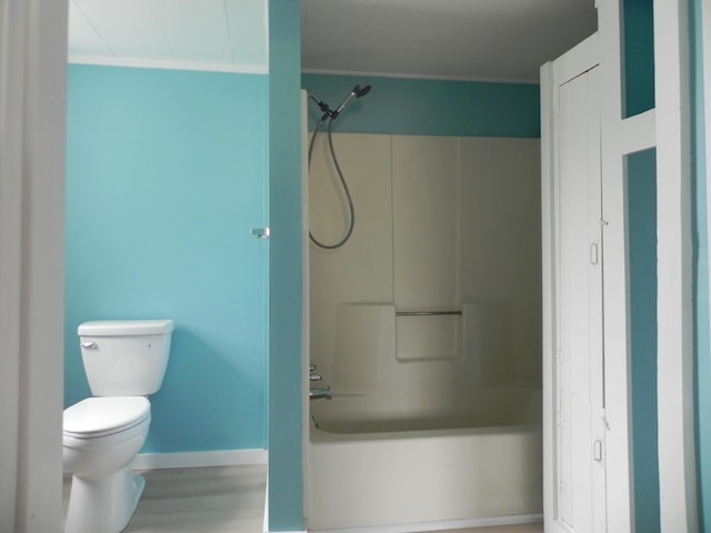 bathroom featuring baseboards, shower / bath combination, wood finished floors, and toilet