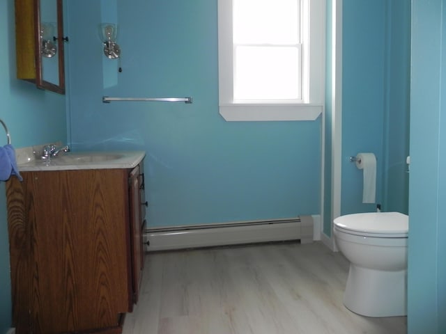 bathroom with a baseboard heating unit, toilet, vanity, and wood finished floors