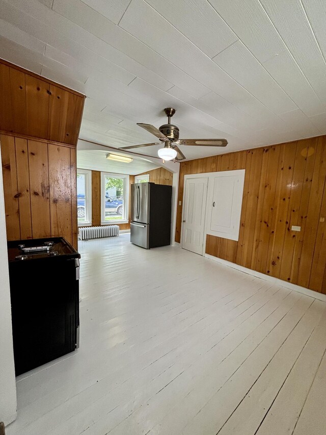 unfurnished living room featuring ceiling fan, light hardwood / wood-style flooring, and wooden walls