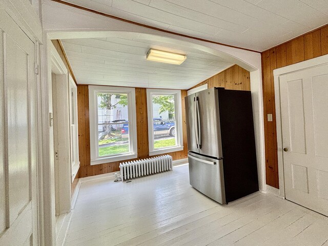 kitchen with radiator heating unit, wooden walls, stainless steel refrigerator, vaulted ceiling, and light hardwood / wood-style floors