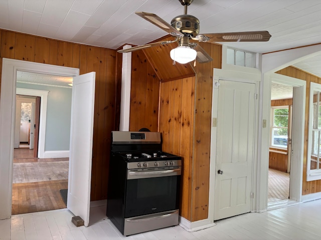 kitchen with ceiling fan, wooden walls, light hardwood / wood-style flooring, and gas range