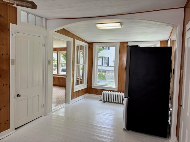 hall featuring lofted ceiling, wooden walls, light wood-type flooring, and radiator heating unit