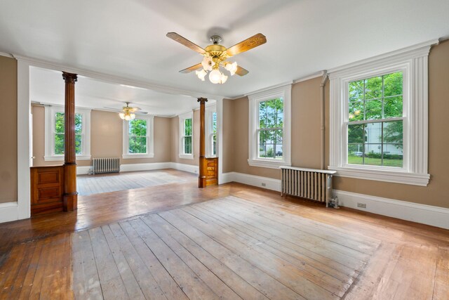 empty room with radiator heating unit, ceiling fan, ornate columns, and hardwood / wood-style floors