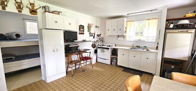 kitchen featuring white range oven, sink, white cabinets, and a healthy amount of sunlight