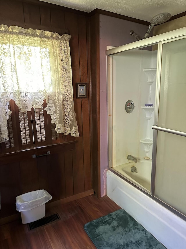 bathroom with hardwood / wood-style floors, enclosed tub / shower combo, wood walls, and a textured ceiling