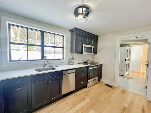 kitchen featuring appliances with stainless steel finishes, sink, stacked washer / drying machine, and light hardwood / wood-style flooring