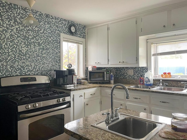 kitchen with stainless steel gas range, a healthy amount of sunlight, white cabinets, and sink