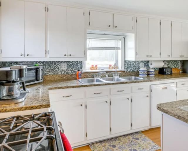 kitchen featuring stainless steel gas range oven, white dishwasher, stone countertops, white cabinets, and sink