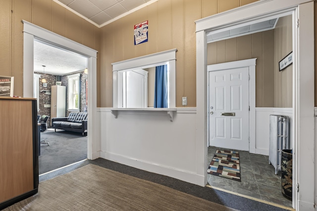 interior space with wooden walls, crown molding, and dark colored carpet