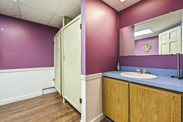 bathroom featuring wood finished floors, vanity, baseboards, and a paneled ceiling