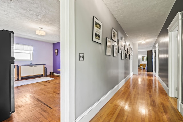 corridor featuring hardwood / wood-style floors, baseboards, and a textured ceiling